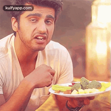 a man is sitting at a table holding a plate of food .