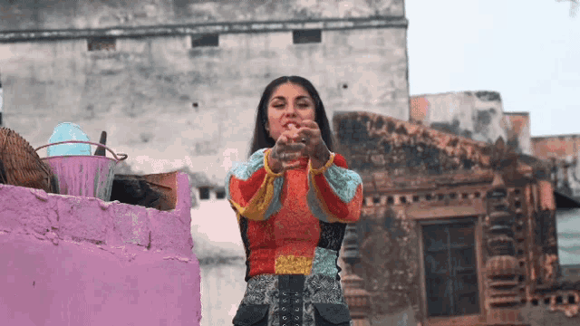 a woman in a colorful sweater is standing in front of a pink building
