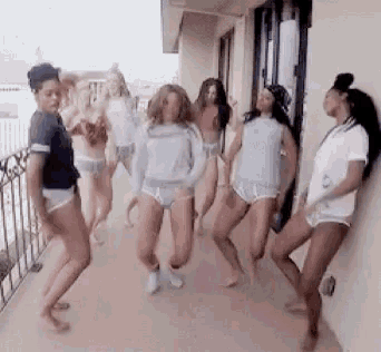 a group of women are dancing on a balcony while one woman leans against a wall .