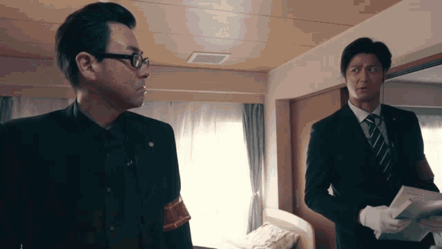 two men in suits and gloves are standing in a bedroom
