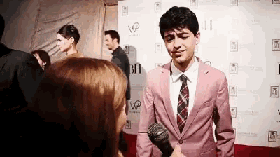 a young man in a pink suit and tie is being interviewed by a woman on a red carpet .