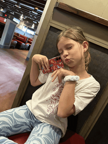 a young girl with a peace sign on her shirt holds a cell phone