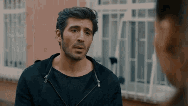 a man in a black hoodie stands in front of a building talking to another man