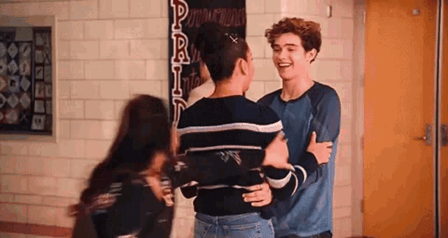 a group of people are hugging each other in a hallway in a school .