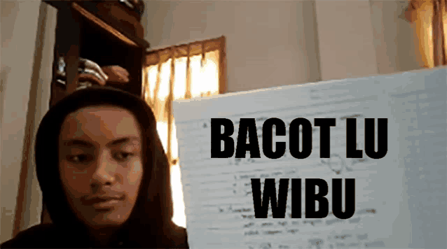 a man in a black hoodie stands in front of a sign that says bacot lu wibu
