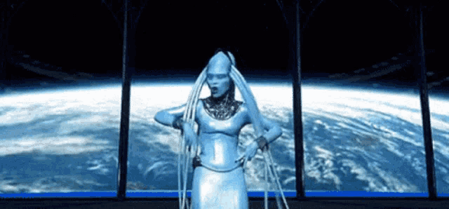 a woman in a silver dress is standing in front of a window looking out to the earth