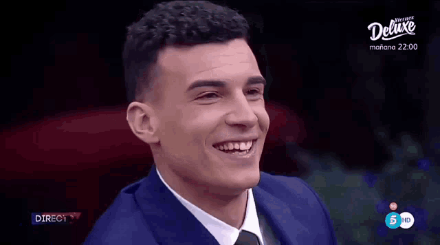 a man in a blue suit and tie is smiling in front of a screen that says directo