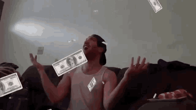 a man is sitting on a couch with his arms outstretched while money is falling from the ceiling .