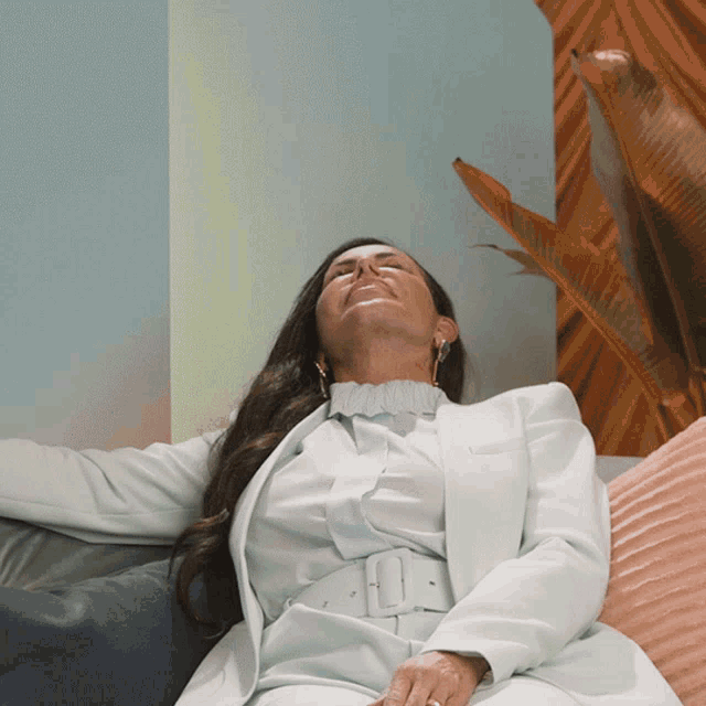 a woman in a light blue suit sits on a couch with her eyes closed