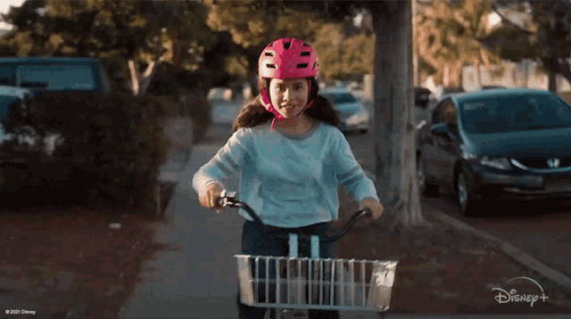 a girl wearing a pink helmet is riding a bike on a sidewalk with a disney logo behind her