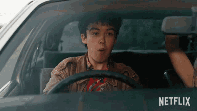 a young man is driving a car with a netflix logo on the side