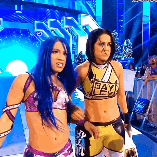 two female wrestlers are standing next to each other with one wearing a yellow top that says bayley
