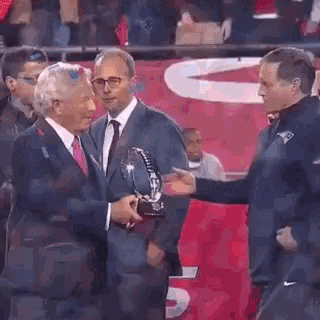 a man in a suit and tie is giving a trophy to another man .