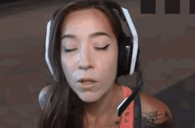 a woman wearing headphones and a pink tank top is looking at the camera .