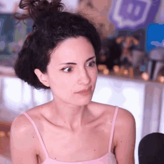 a woman in a pink tank top is sitting in a room with a bun in her hair .