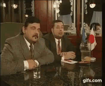 two men in suits and ties are sitting at a table with the words wat you written on the table .