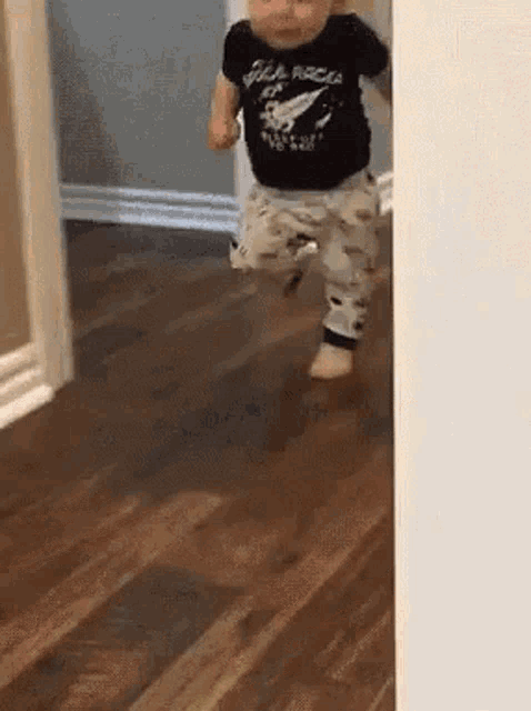 a baby is walking on a wooden floor wearing a black shirt that says rock on .