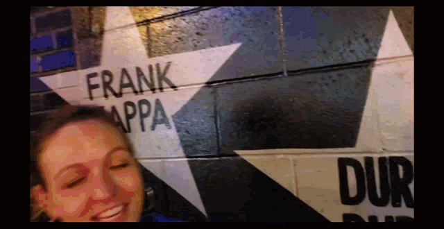 a woman is smiling in front of a wall that has frank appa painted on it