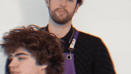 a man wearing a purple apron is cutting a man 's hair .