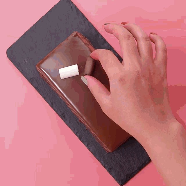 a person holding a piece of marshmallow on top of a chocolate cake