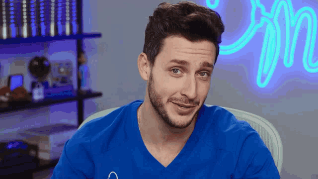 a man in a blue shirt is sitting in front of a neon sign
