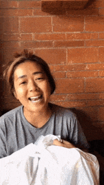 a woman in a grey shirt is smiling and holding a white bag