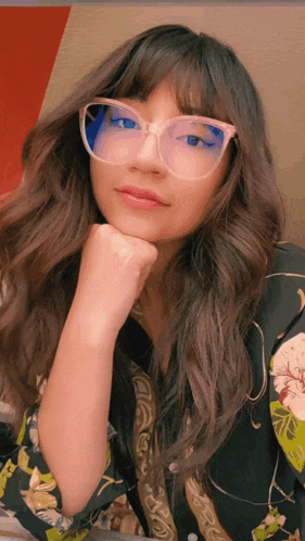 a woman wearing glasses and a floral shirt is looking at the camera