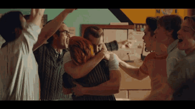 a group of people are hugging each other in front of a sign that says m