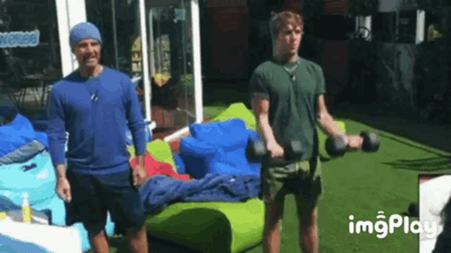 a man is lifting a dumbbell while another man stands behind him .