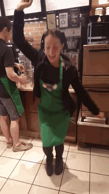 a woman in a green apron is dancing in front of a sign that says price match