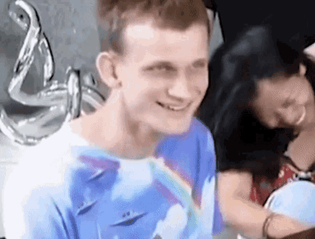 a man in a blue shirt is smiling while sitting next to a woman in a red dress .