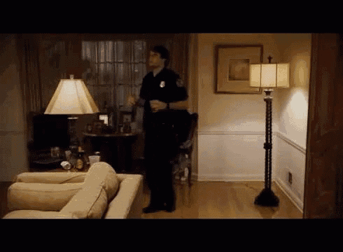 a police officer is standing in a living room holding a baton .