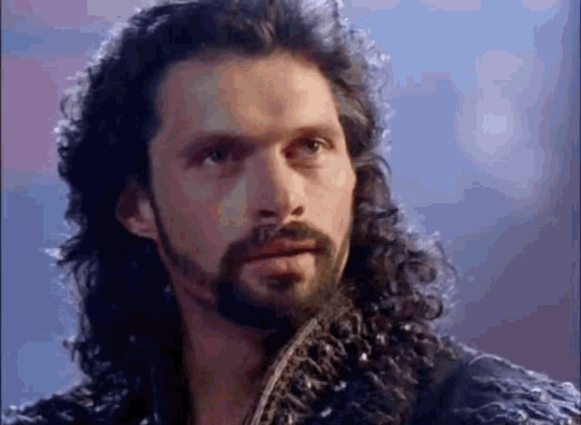 a man with long hair and a beard is looking at something .