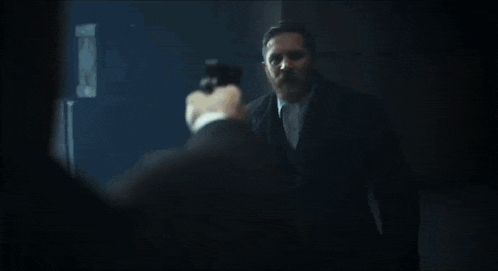 a man in a suit and tie is standing in a dark room and talking .