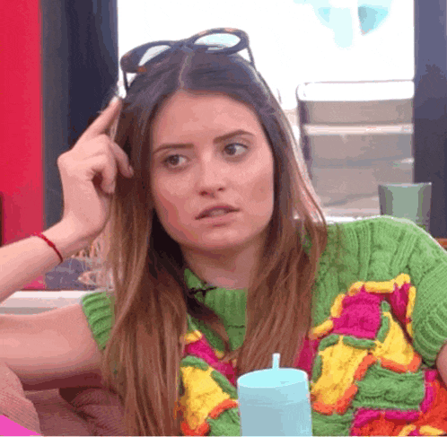 a woman wearing sunglasses and a green sweater scratches her head