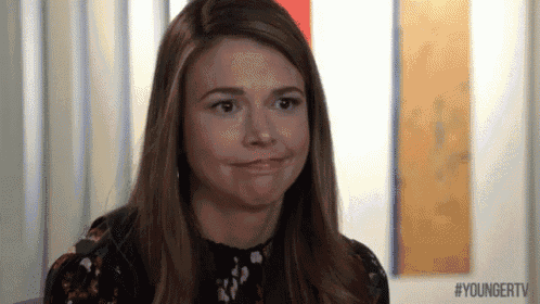 a woman is making a funny face while sitting in front of a wall with paintings on it .