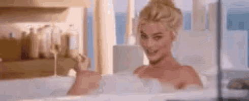 a woman is taking a bath in a bathtub filled with foam and holding a glass of champagne .