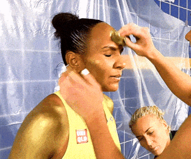 a woman in a yellow tank top with a red ucla logo on it is getting her face painted gold