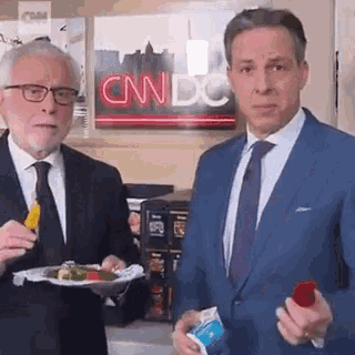 two men are standing next to each other in front of a cnn dc sign .