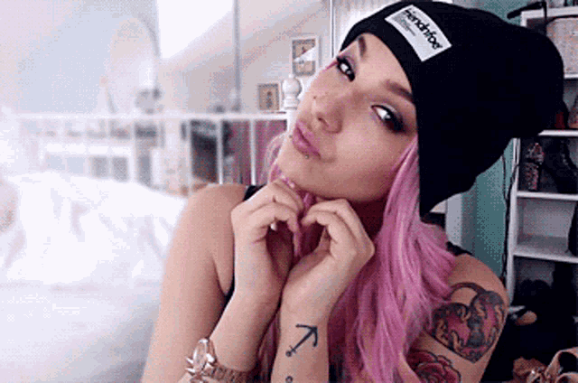 a woman with pink hair wearing a black beanie that says french kiss on it
