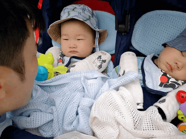 a man holds two babies in a stroller with one wearing a hat that says ' sheep ' on it