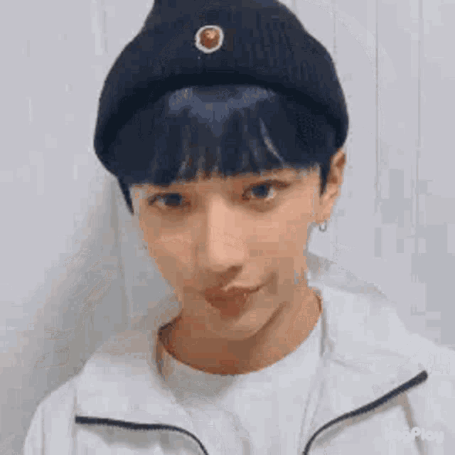 a young man with blue hair is wearing a black beanie and a white shirt .