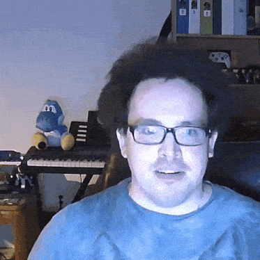 a man wearing glasses is sitting in front of a keyboard and a stuffed animal