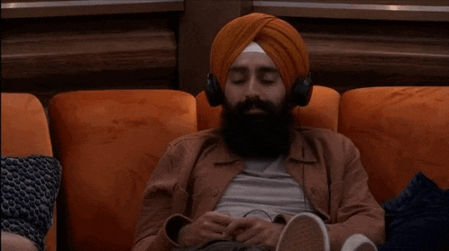 a man with a beard is sitting on a couch wearing headphones and a turban .