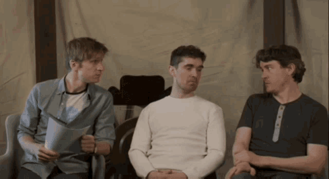 three men are sitting in chairs one of whom is holding a piece of paper