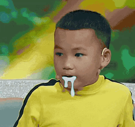 a young boy wearing a yellow shirt has a white liquid coming out of his mouth .
