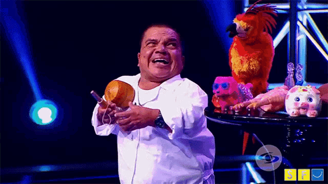 a man in a white shirt is standing on a stage with stuffed animals including a pig and a parrot
