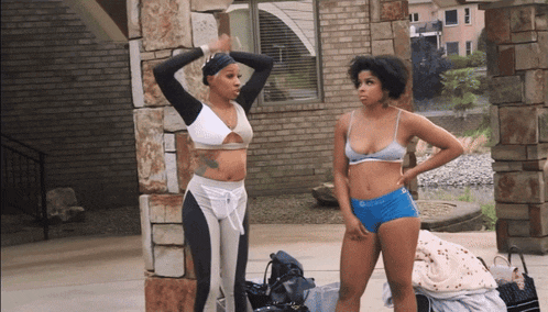 two women standing in front of a brick building one is wearing a bikini top and shorts that say calvin klein