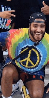 a man wearing a tie dye shirt with a peace sign on it is smiling
