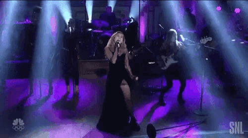 a woman in a black dress is singing into a microphone on stage